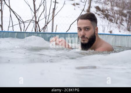 Jeune homme souriant s'amusant en nageant dans une glace piscine en hiver Banque D'Images