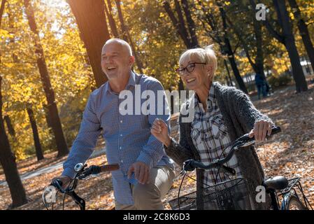 Joyeux couple senior souriant à vélo dans le parc d'automne une journée ensoleillée Banque D'Images