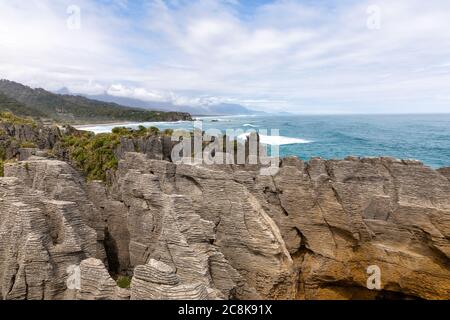 Le célèbre Pancake Rocks sur Dolomite point avec une vue sur la mer vers les montagnes couvertes de nuages. Dolomite point, Île du Sud, Nouvelle-Zélande Banque D'Images