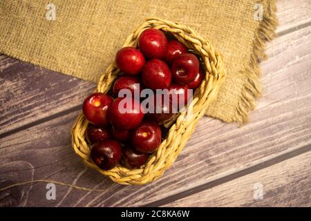 Cerises mûres juteuses dans un panier en osier sur un fond de tissu de maison avec une texture rugueuse. Gros plan Banque D'Images