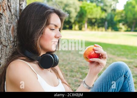 belle jeune femme caucasienne assise sur l'herbe près de l'arbre avec la pomme rouge dans les mains Banque D'Images