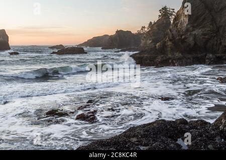 Le soleil se couche sur Secret Beach, sur la côte sud de l'Oregon, au coucher du soleil, avec ses nombreux îlots recouverts d'arbres à feuilles persistantes et de vagues floues qui se déplacent vers l'intérieur Banque D'Images