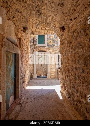 Entouré de pierre. Une petite tache de soleil éblouissante et une porte abîmé au bout d'une allée voûtée dans la ville médiévale de Pyrgi, île de Chios, Grèce. Banque D'Images