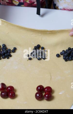 Les cerises et les bleuets, empilés en piles, se trouvent sur la pâte à pâte. Cuisson des boulettes. Banque D'Images