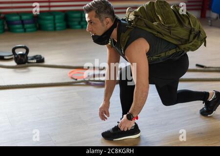 Un instructeur motivé s'agenouille et attache ses chaussures avec un sac à dos et un masque d'entraînement. Commencer la formation. Pour le camp de chaussures et le concept de gym. Banque D'Images