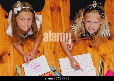 Deux filles caucasiennes ayant l'amusement et le dessin couché sur le plancher en bois, regardant vers le haut. Activités de loisirs Banque D'Images