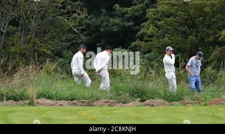 Les joueurs et un spectateur recherchent le ballon perdu dans la longue herbe lors du match de Birch Vale et Thornsett contre Old Glossop dans le Derbyshire et Cheshire Cricket League Div 2 premier match de la saison, tronqué en raison de la pandémie du coronavirus. Banque D'Images