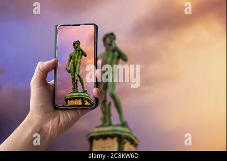 Touriste prenant une photo de la réplique de la statue du David de Michel-Ange sur la place Michel-Ange pendant le coucher du soleil à Florence, Italie. Homme tenant le téléphone et prenant Banque D'Images