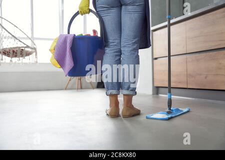 Lavage du sol. Vue arrière d'une femme tenant une vadrouille et un seau en plastique ou un panier avec des chiffons, des détergents et différents produits de nettoyage tout en étant debout dans la cuisine moderne. Nettoyage, ménage, ménage Banque D'Images