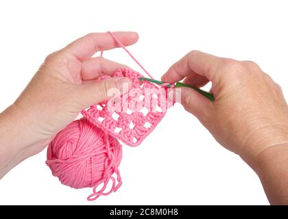 Les femmes caucasiennes matures crochoquant les mains de fils roses vibrants dans le motif carré granny, isolé sur blanc. Gros plan. Banque D'Images