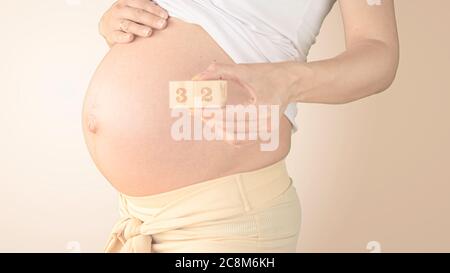 Jeune femme enceinte avec numéro de semaine de grossesse à côté de son ventre. Photos de la croissance du ventre à 32 semaines de grossesse. Alimentation saine pendant la grossesse Banque D'Images