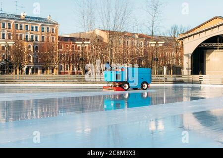 Préparation de la glace à la patinoire entre les séances de la journée ensoleillée d'hiver/ glace polie prête pour le match/ machine d'entretien de glace en mouvement, vue latérale. Banque D'Images