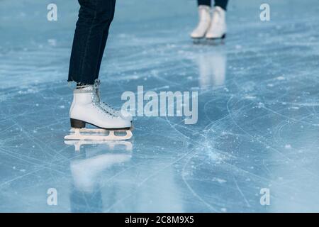 Gros plan sur les jambes du patineur sur la patinoire extérieure. Femme se tient dans des patins blancs. Activités en extérieur le week-end par temps froid. Banque D'Images