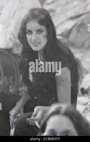 Fin années 70 vintage noir et blanc style de vie photographie d'une belle jeune femme souriante regardant l'appareil photo. Banque D'Images