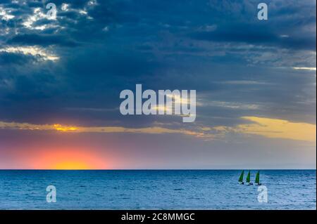 Coucher de soleil doré sur la magnifique plage de Brighton Beach à Adélaïde, en Australie méridionale, trois voiliers se déplacent vers le soleil couchant sur l'océan sud. Banque D'Images