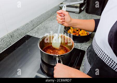 Les mains préparant le caramel sur une cuisinière à induction à côté d'un bol de pommes pour un gâteau Banque D'Images