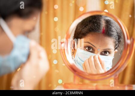 Femme indienne se préparer devant le miroir en ajustant le masque médical avant de sortir pendant la fête - concept de nouvelle normale due à Banque D'Images