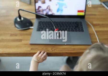 Une fille s'assoit sur une chaise et joue dans un jeu en ligne avec un ordinateur portable et un microphone sur une table à la maison. Banque D'Images