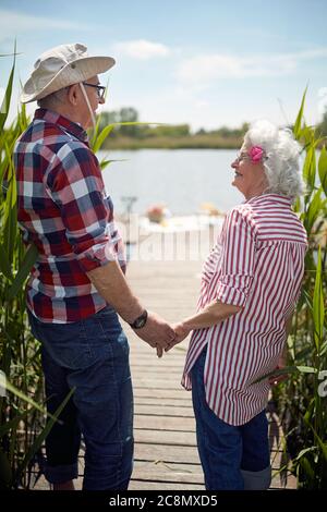 gros plan de couple caucasien vieux tenant les mains, regardant l'un l'autre, souriant, debout au bord du lac Banque D'Images