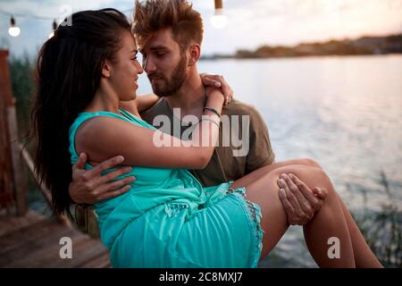 jeune homme de barbe tenant dans les bras belle femme, au bord de la mer au coucher du soleil. couple romantique amoureux Banque D'Images