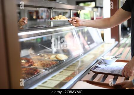 L'homme se tient derrière le comptoir de la nourriture prête à l'emploi dans la salle à manger et tient l'assiette avec le déjeuner dans sa main. Banque D'Images