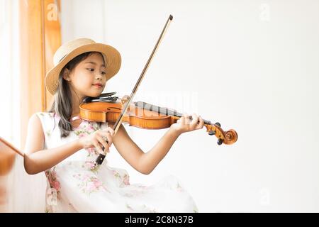 Une mignonne fille d'école élémentaire asiatique joue un violon heureusement dans sa maison. Banque D'Images