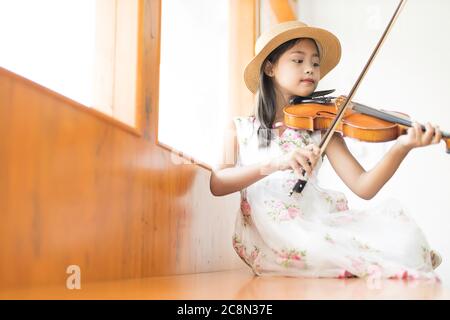 Une mignonne fille d'école élémentaire asiatique joue un violon heureusement dans sa maison. Banque D'Images