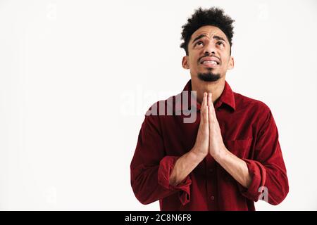 Photo d'un jeune homme africain nerveux plein d'espoir posant isolé sur fond de mur blanc montrant prier s'il vous plaît geste Banque D'Images