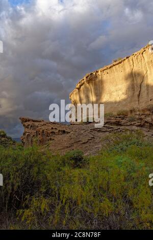 Roches volcaniques et couches de cendres formant des falaises abruptes sculptées par l'eau, tour au-dessus d'une vallée pleine de succulents et de buissons à la lumière du soleil du soir. Banque D'Images