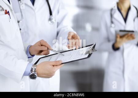 Des médecins inconnus, deux hommes et une femme, discutent des examens médicaux, tout en se tenant au bureau de l'hôpital. Médecins utilisant des planches à découper pour remplir Banque D'Images