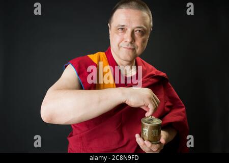 Le moine tient un tambour de prière dans sa main. Portrait d'un moine bouddhiste en vêtements rouges. Banque D'Images