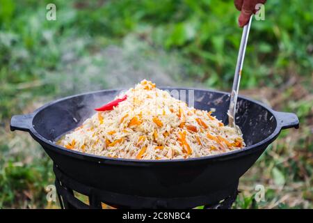 Cuisson du riz pilaf dans un grand pot en fonte au feu Banque D'Images