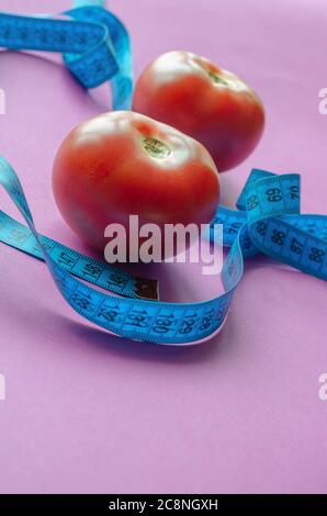 Ruban de mesure bleu et tomates mûres. Deux tomates rouges en gros plan. Régime, perte de poids, concept de forme physique. Photo inclinée. Mise au point sélective. Banque D'Images