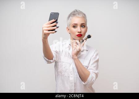 Portrait de studio de belle fille à la mode avec les cheveux courts en tenant par téléphone cellulaire selfies over white background isolés Vloger Blogger maquilleur Banque D'Images