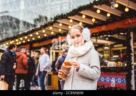 Une petite fille mignonne mange une pâtisserie hongroise traditionnelle appelée Kurtoskalacs à Budapest sur le marché de la rue l'hiver Banque D'Images