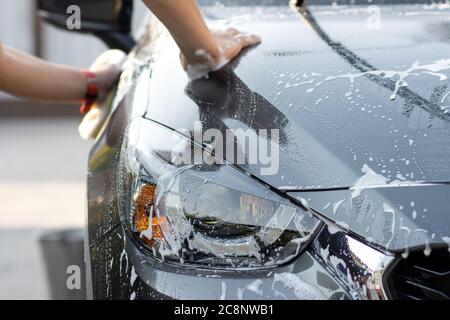 Laver la voiture à la main à l'eau savonneuse. L'homme nettoie la voiture avec une éponge, de l'eau et du détergent. Banque D'Images