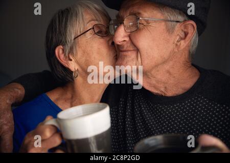 Un couple senior heureux s'embrasse et rit tout en buvant du café. Banque D'Images