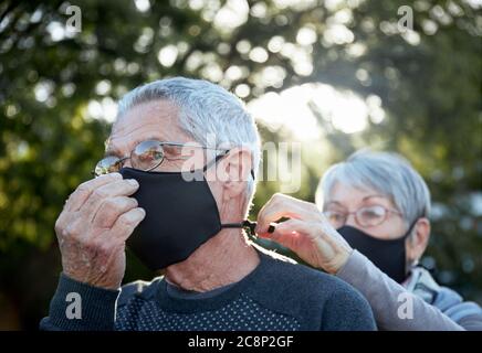 Couple senior actif sur la marche extérieure portant des masques faciaux. Femme aidant l'homme avec le masque. Banque D'Images