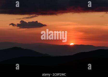 Un coucher de soleil éblouant avec un disque circulaire du soleil sur les contours des montagnes et des nuages illuminés dans le ciel Banque D'Images