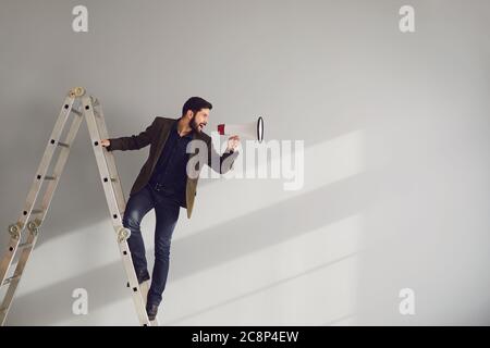 Un homme d'affaires barbu dans les escaliers avec un mégaphone dans les mains se déchèrent sur un fond gris. Banque D'Images