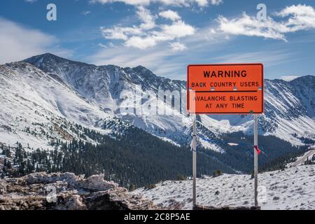 Rouge vif/orange signe lecture Avertissement avalanches explosion dans la zone montanesque avec neige couvert montagnes en arrière-plan Banque D'Images