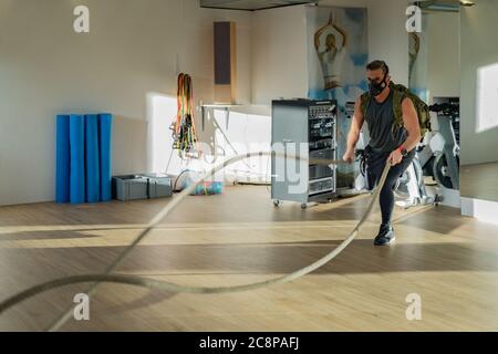 Sportif à l'entraînement de corde avec masque d'entraînement. Intérieur sur parquet en chêne avec soleil et ombre. Pour le concept de camp de démarrage. Banque D'Images