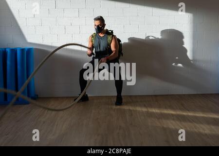 Sportif à l'entraînement de corde avec masque d'entraînement. Intérieur sur parquet en chêne avec soleil et ombre. Pour le concept de camp de démarrage. Banque D'Images