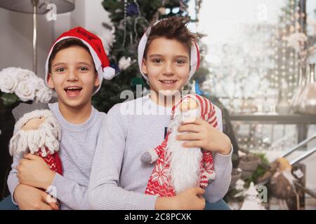 Heureux petits frères jumeaux riant, portant des chapeaux de Père Noël appréciant célébrer Noël Banque D'Images