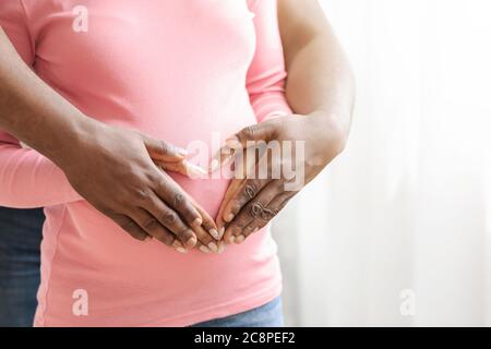 Gros plan sur un couple africain non reconnaissable qui met les mains sur le ventre Banque D'Images