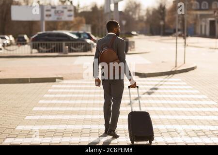 Homme d'affaires noir méconnu avec Suitcase Crossing Road à City, vue arrière Banque D'Images