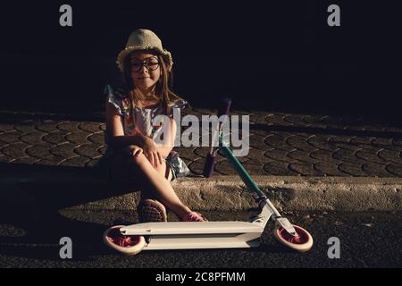 portrait d'une petite fille assise à côté de son scooter à deux roues. Photo de haute qualité Banque D'Images