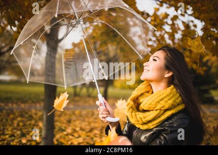 Jolie fille gaie brune dans le parc d'automne avec parapluie - le vent porte des feuilles jaunes - couleurs d'automne Banque D'Images