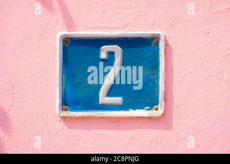 Deux, numéro 2, plaque bleue sur surface rose. Banque D'Images