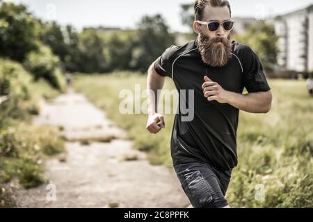 Jeune heureux joyeux souriant barbu, pendant le jogging matinal dehors. Banque D'Images
